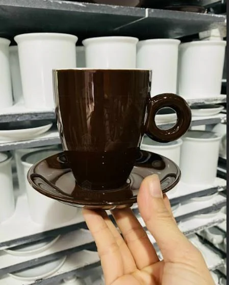 Cốc men nâu quai tròn cùng đĩa kê được cầm trước kệ cốc