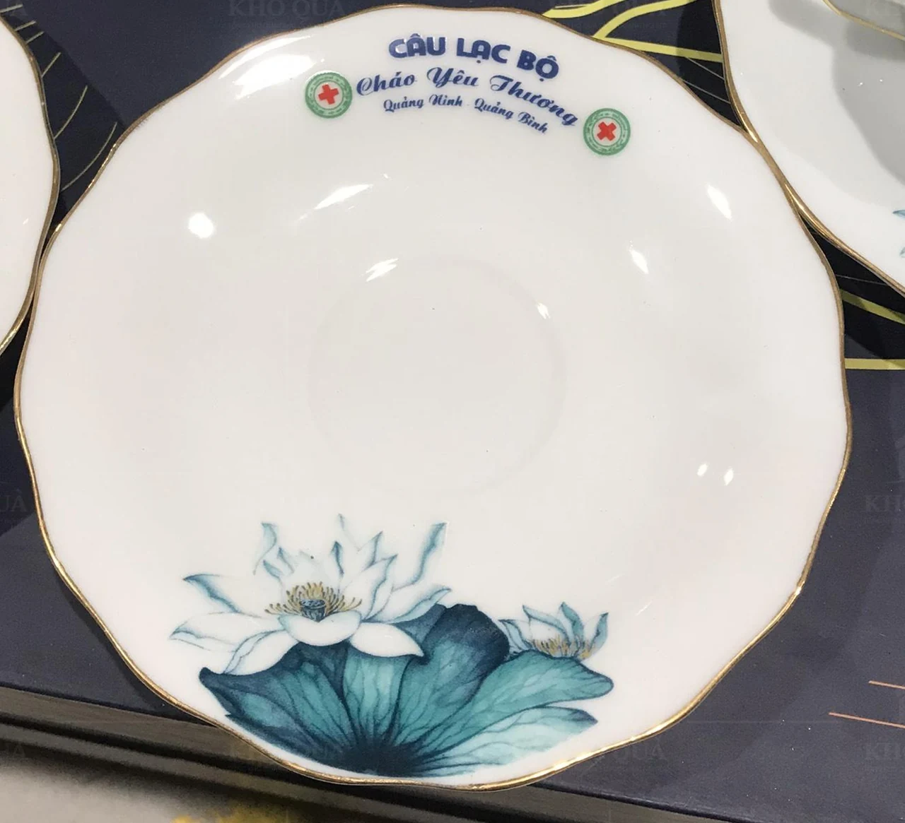 Đĩa viền vàng có tên câu lạc bộ ở trên và hoa sen ở dưới