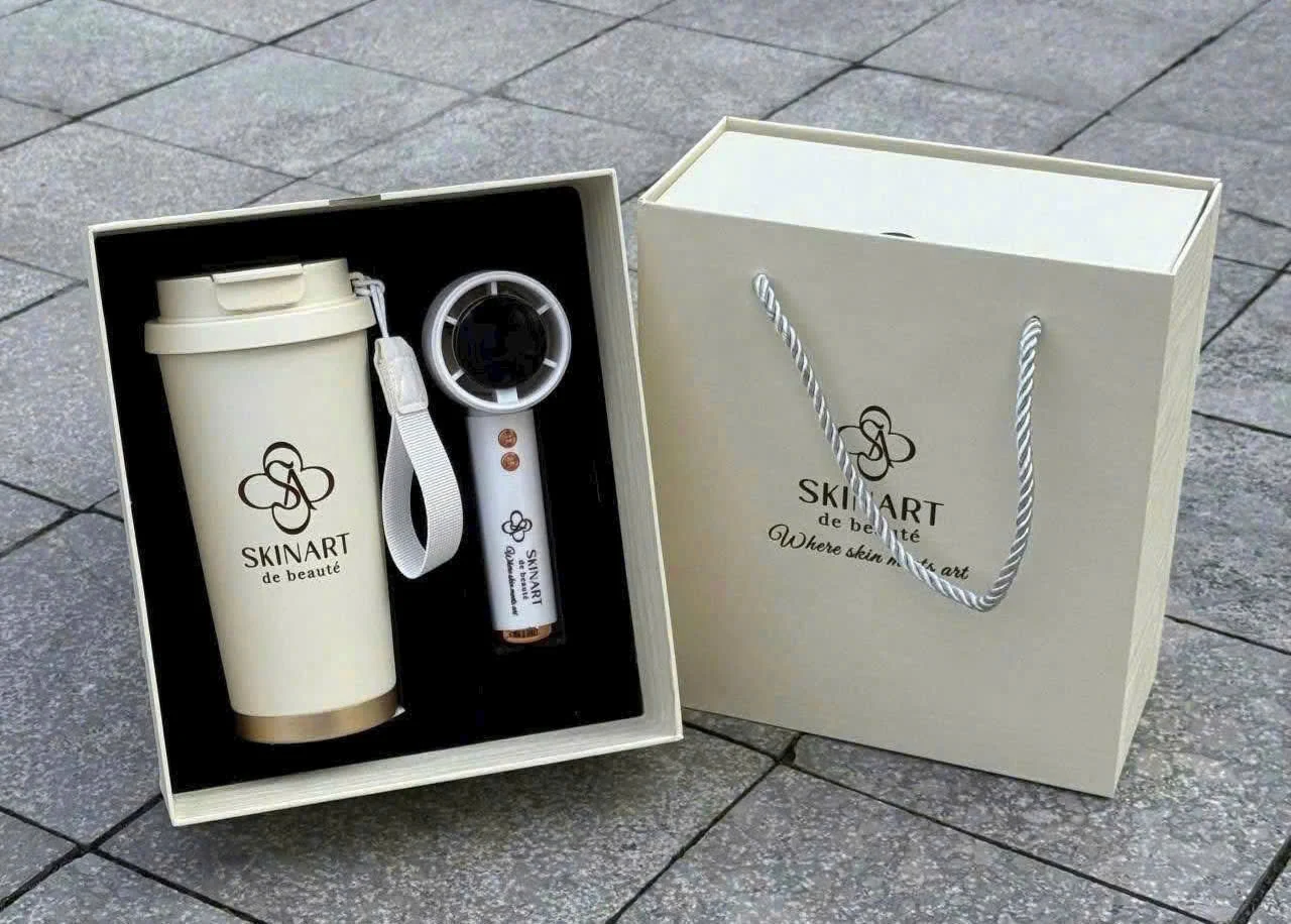 Ly, thiết bị cầm tay và túi cùng logo SKINART trong bộ quà