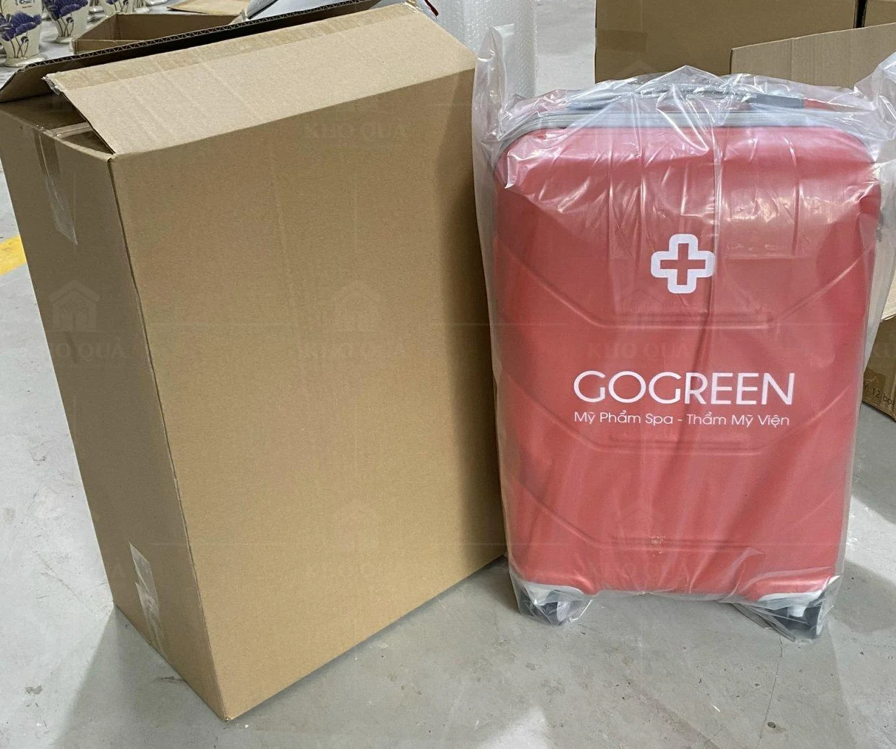 Vali đỏ in GOGREEN trong túi bảo vệ đặt cạnh thùng carton