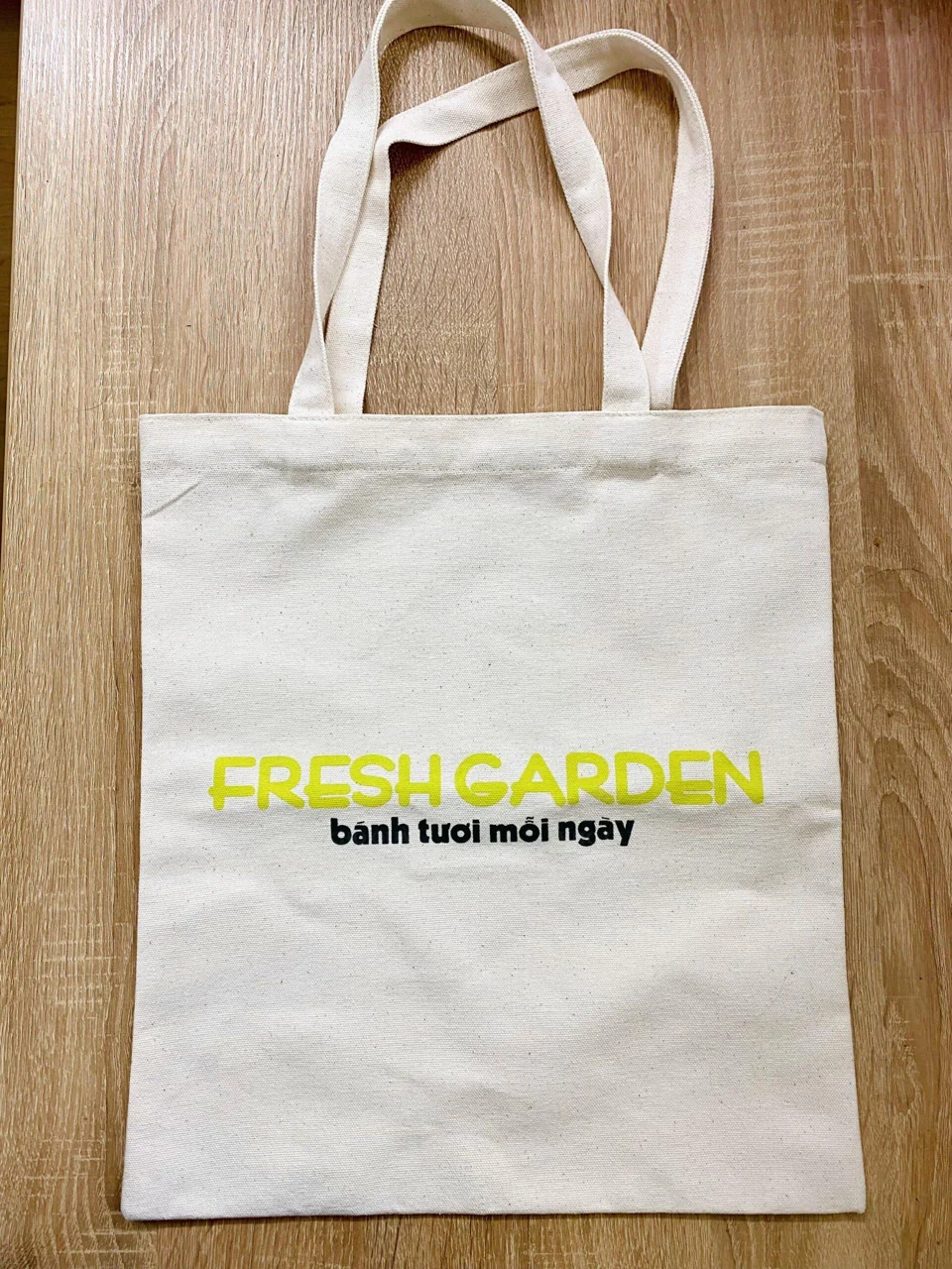 Túi canvas sáng màu in Fresh Garden nằm trên mặt gỗ